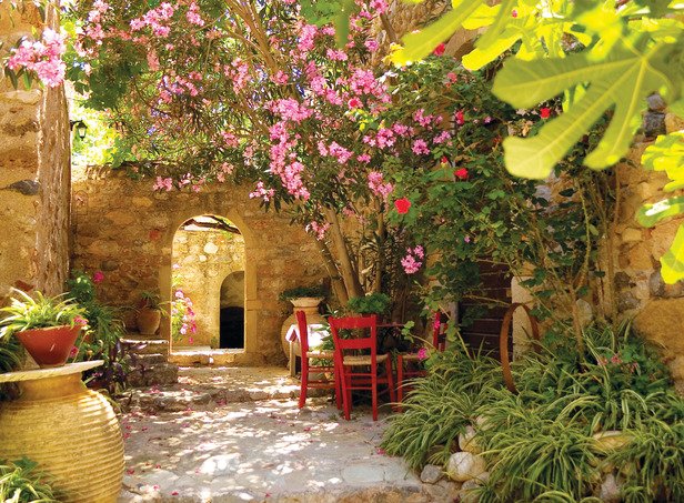 Czerwone krzesła, gliniane donice i jasne, kamienne mury – nawet bez palm można wykreować w ogrodzie śródziemnomorski klimat. 